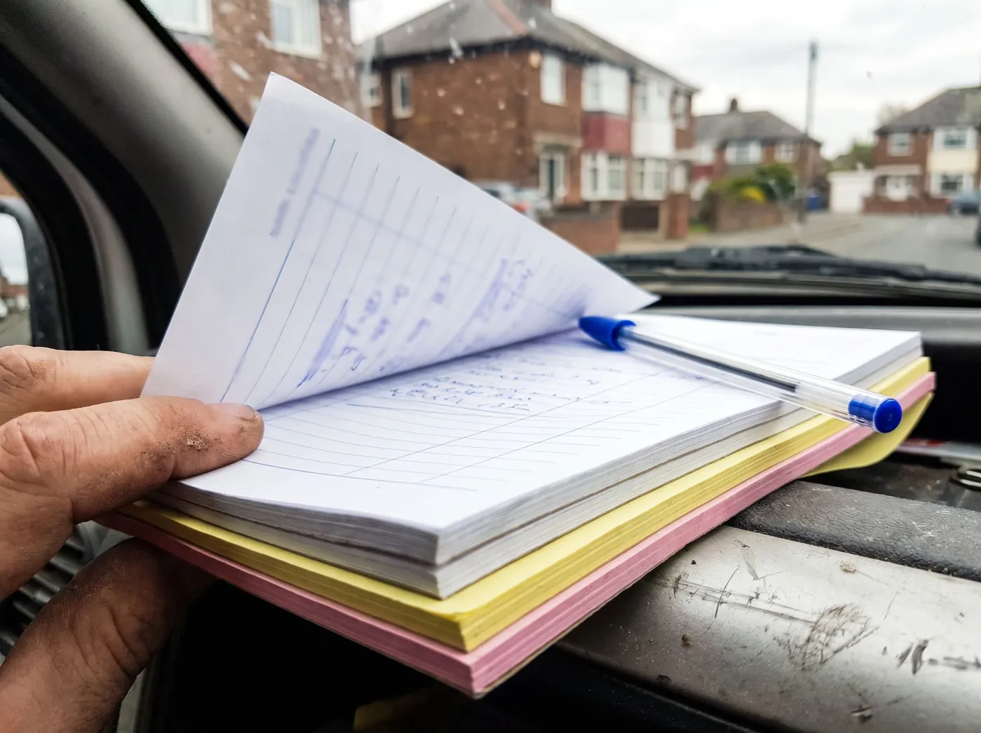 A hand holding a duplicate job pad in a van