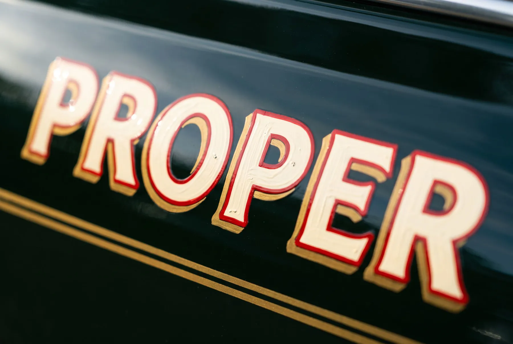 Close-up of hand-painted cream lettering with a gold drop-shade on a green panel